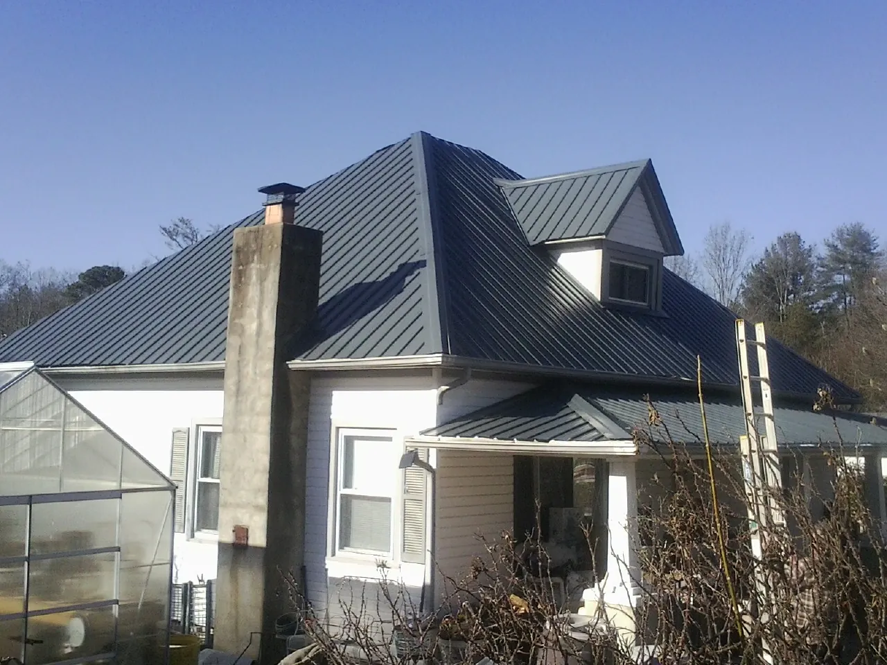 Dark blue standing seam metal roof on a white farmhouse with dormer — Slate & Tile Roof Repair by Roofing Brothers in Severance
