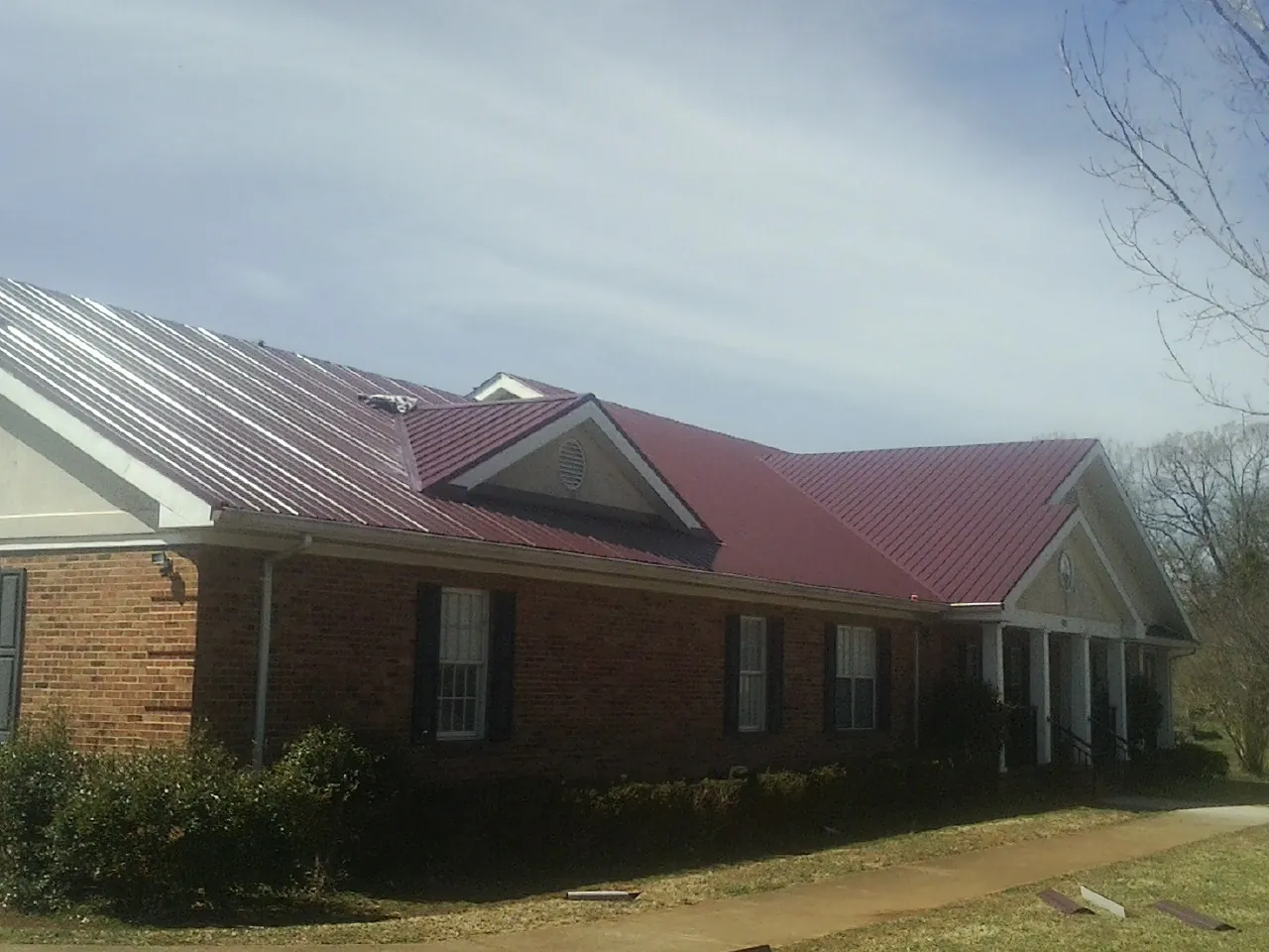 Red metal roof with gabled entries on a long brick building, from a Hail Damage Roof Repair job in Severance