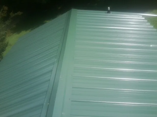 New green metal panels meeting at the ridge of a roof — Flat Roof Repair work by our crew in Severance