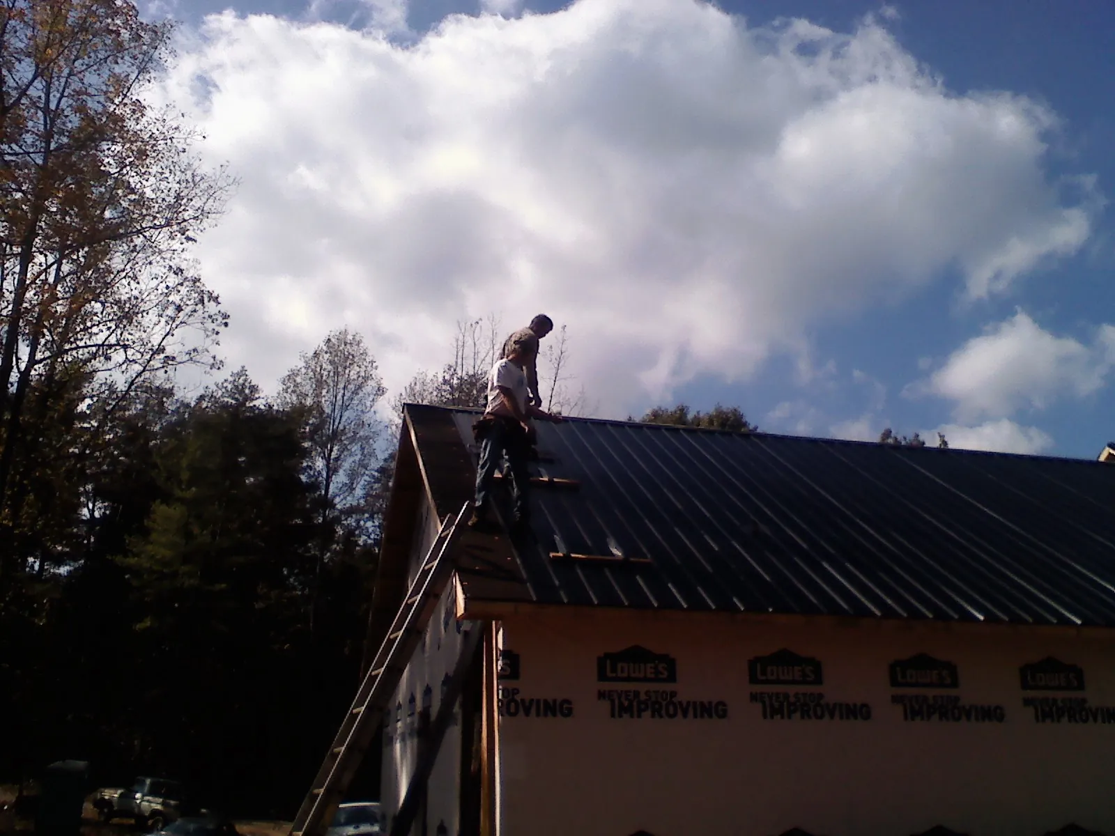 Roofer fastening dark metal panels high against a cloudy sky, from a Roof Inspection job in Severance