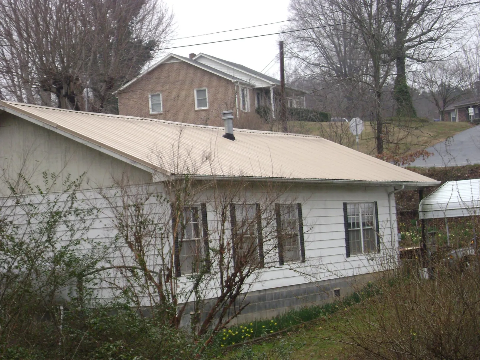 Tan metal roof on a white sided house set into a hillside — Commercial Roofing by Roofing Brothers in Severance