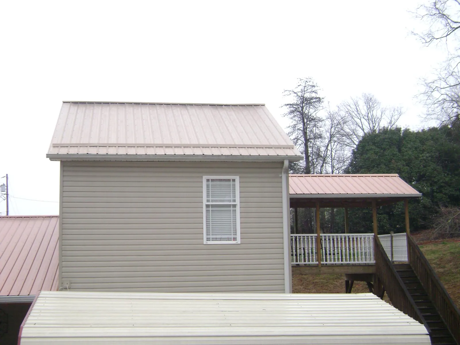 Tan metal roofs on a two story addition and attached porch, from a Roof Replacement job in Severance
